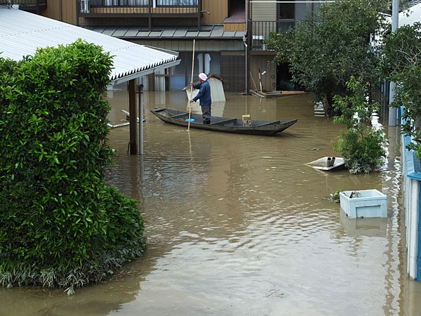 堤防から浸水した自宅まで小船で移動する人